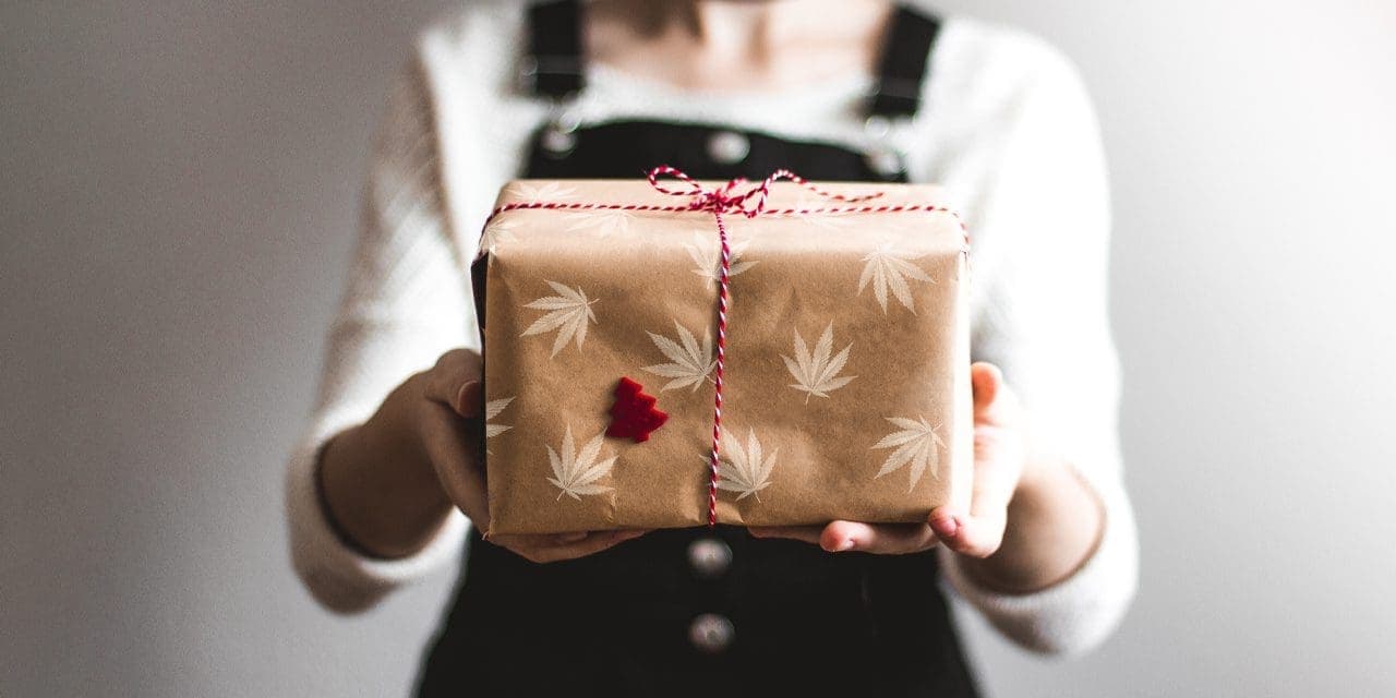 a woman holding out a brown cannabis printed box with string ribbon