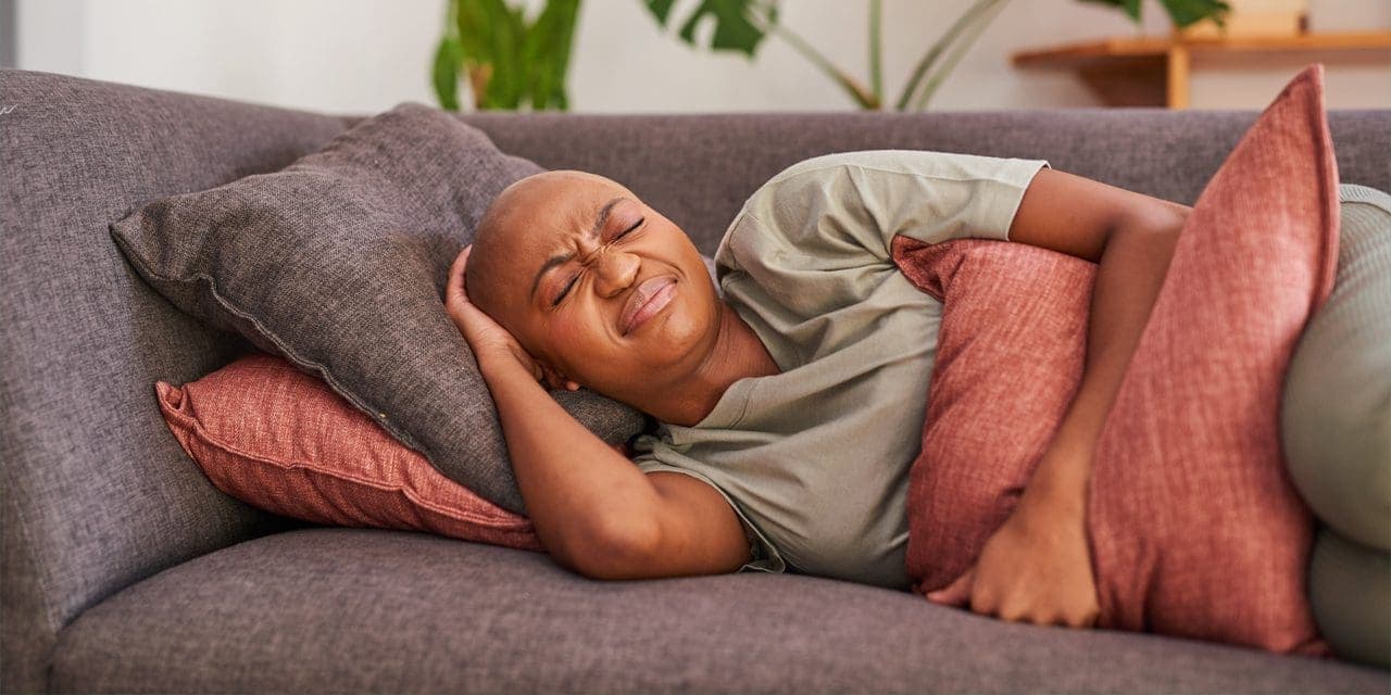 bald woman laying in pain clutches her stomach